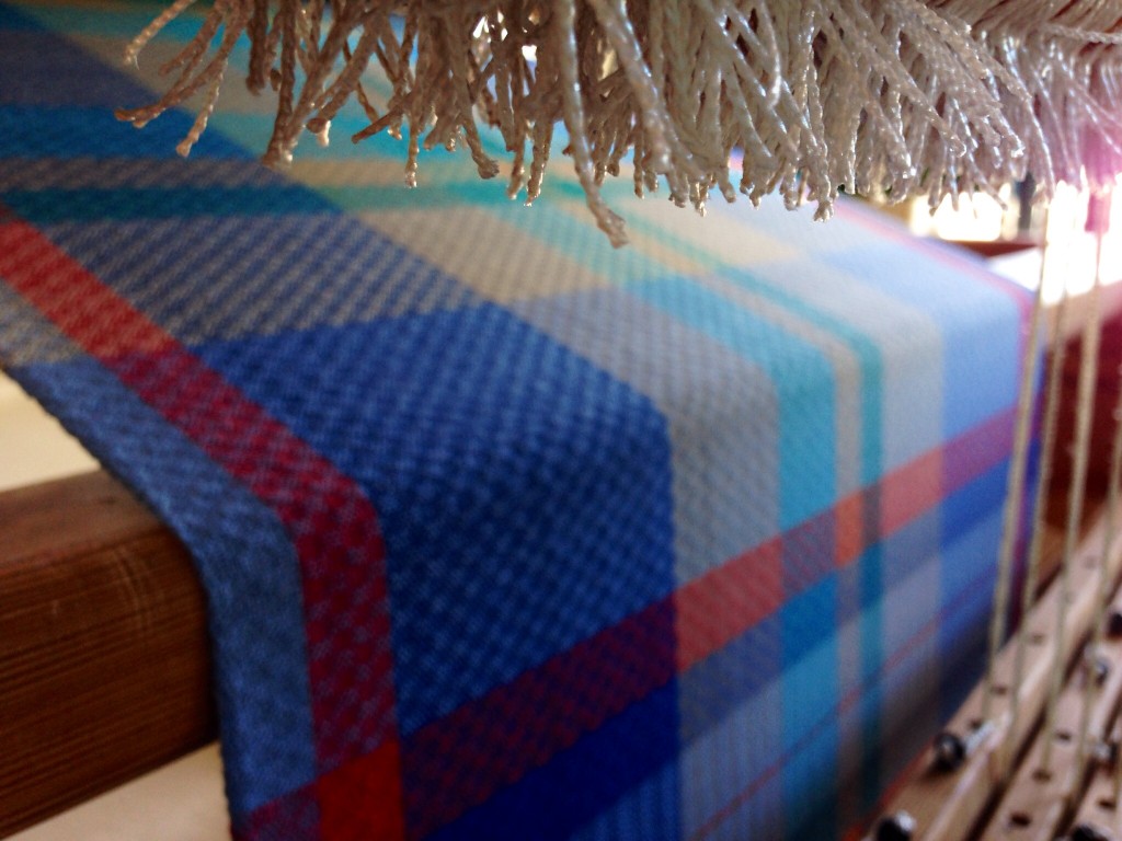 Cut ends of the heddles are in focus, viewed from back of loom under the warp.