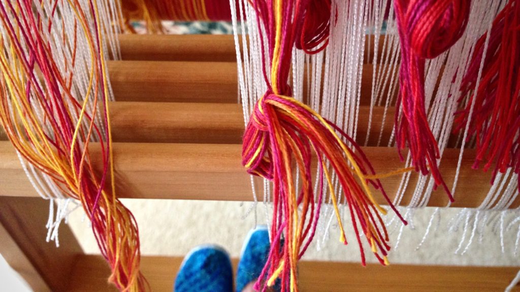 Threading brightly-colored warp for handwoven baby wrap.