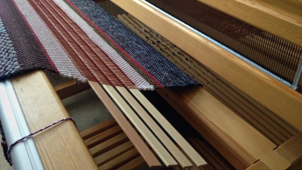 Warping slats are used as spacers between two rag rugs on the loom.