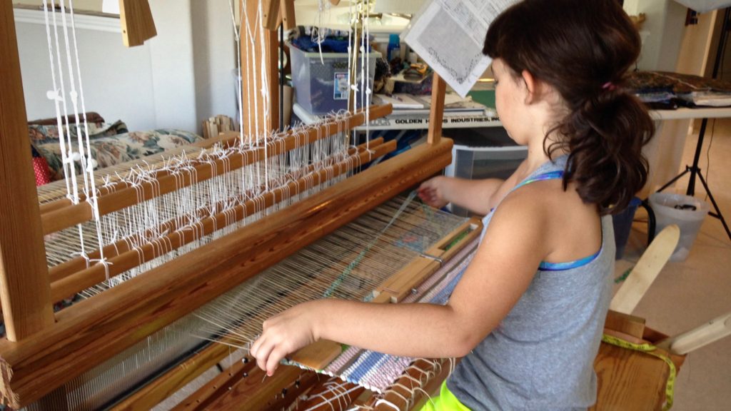 Young weaver at the loom making her first rag rug.