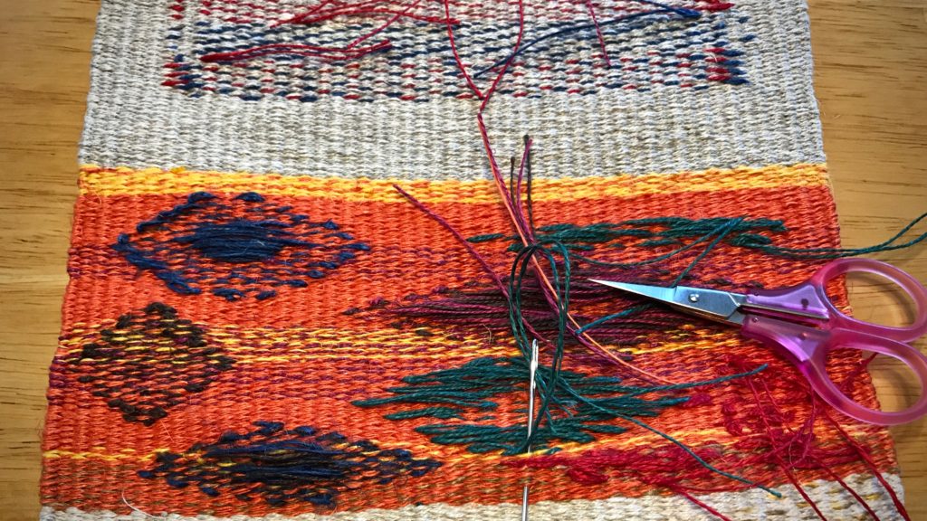 Sewing in weft tails in the back of a tapestry.