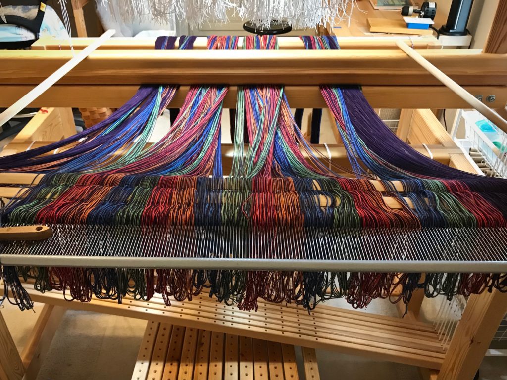 Pre-sleying the reed at the loom.