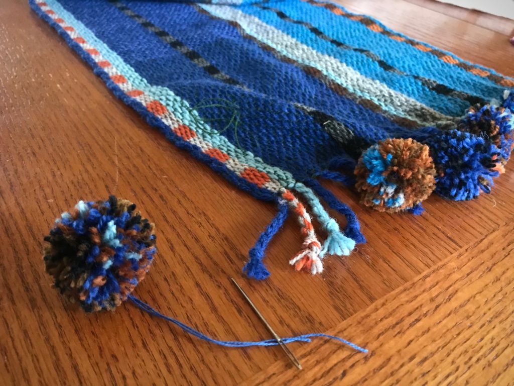 Adding pompom embellishments to the scarf.