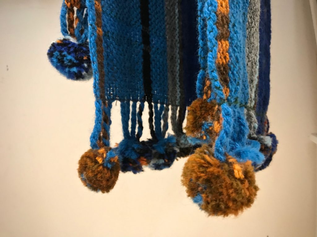 Handwoven scarves with pompoms, hanging to dry.