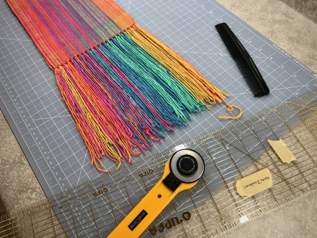 Trimming fringe on a handwoven scarf.